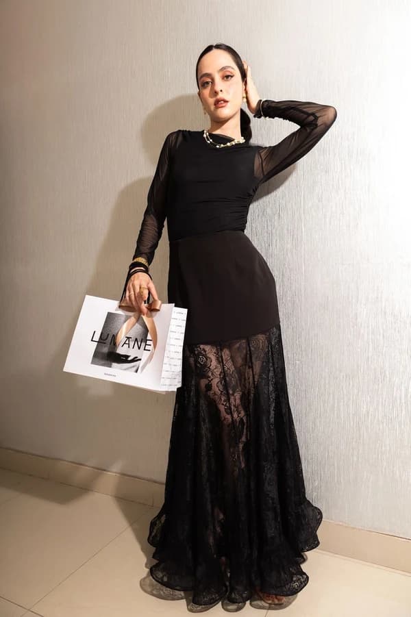Modelo con vestido largo de encaje negro y top semitransparente de manga larga, sosteniendo una bolsa de compras LUMANE.